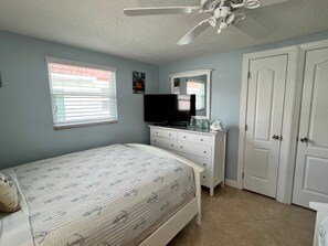 Ein Schlafzimmer mit Bett, Kommode, Fernseher und Deckenventilator.