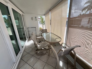 Eine sonnendurchflutete Terrasse mit einem Glastisch und vier Stühlen, einer Schiebetür und Blick ins Freie.
