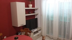 Een woonkamer met een televisie op een dressoir, een rode wand, een wit kastje en een raam met dunne gordijnen.