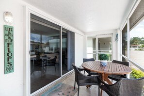 A covered outdoor dining area with a round wooden table and wicker chairs, a sliding glass door leading to a patio, and a sign with motivational text on the wall. - Casa Blanca Villa - VA04 (Sarasota)