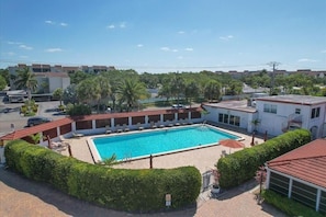 A swimming pool surrounded by greenery, a building with a red roof, and a clear blue sky. - A04 - Let the Beach Be Your Backyard (Sarasota)