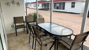 Eine überdachte Terrasse mit einem runden Tisch und sechs Stühlen, mit Blick auf eine Wohngegend mit Häusern und Palmen.