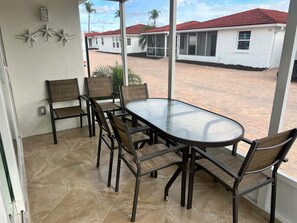 A covered patio with a round table and six chairs, overlooking a residential area with houses and palm trees. - Casa Blanca  - Villa A14 (Sarasota)