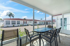 A covered outdoor area with a glass table and chairs, a view of a residential area with houses and palm trees. - Casa Blanca - Villa A14 (Sarasota)
