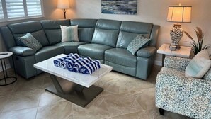 Ein Wohnzimmer mit einem Ecksofa, einem Couchtisch, einem Beistelltisch mit Lampe und einem Bild an der Wand.