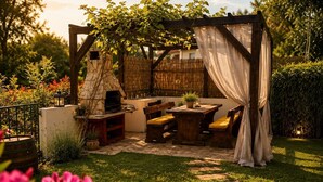 An outdoor patio with a stone fireplace, wooden furniture, and a pergola with white curtains. - House Ivana (Krsan)