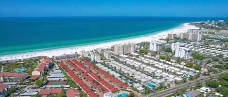 An aerial view of a coastal area with a beach, hotels, and a road.