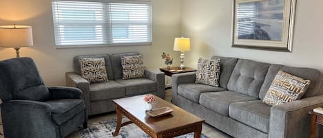 Ein Wohnzimmer mit grauem Sofa, Sesseln, einem Couchtisch und einem Teppich.
