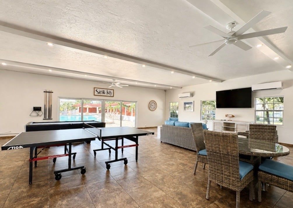 Une pièce équipée de tables de ping-pong, d’un canapé, de fauteuils en osier, d’un ventilateur de plafond et d’un téléviseur.