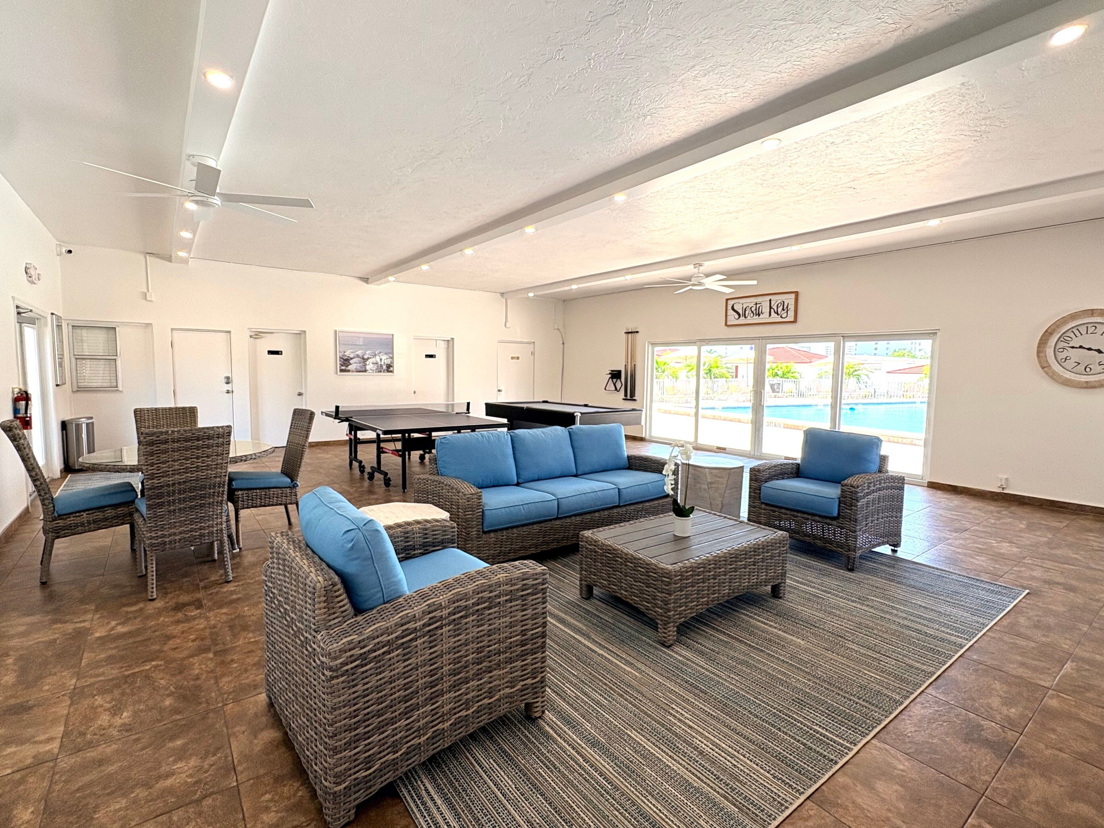 A spacious indoor area with wicker furniture, a pool table, and a ceiling fan.