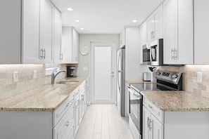 A modern kitchen with white cabinets, granite countertops, stainless steel appliances, and a clock on the wall. - Casa Blanca - Villa B08 (Sarasota)