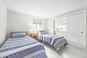 A bedroom with two beds, a nightstand, a lamp, and a dresser. - Casa Blanca - Villa B14 (Sarasota)