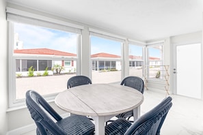 A sunlit patio with a round table and four chairs, large windows, and a view of a red-tiled roof building. - Casa Blanca - Villa B14 (Sarasota)
