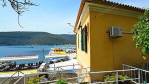 Un edificio giallo con un balcone che si affaccia su una marina con barche e un paesaggio collinare sullo sfondo.