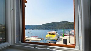 Vista dalla finestra su una marina con barche ormeggiate, cielo sereno e paesaggio collinare sullo sfondo.