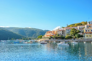 A coastal town with buildings along the waterfront, boats docked in the water, and a hilly landscape in the background. - Apartment Rajan (Labin)