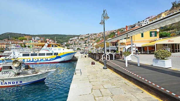 Una zona sul lungomare con barche ormeggiate, una passeggiata pedonale e edifici sullo sfondo.