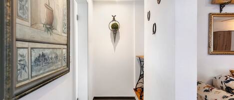A hallway with a framed artwork, a hanging plant, a black metal bench, and a sofa with a floral pattern.