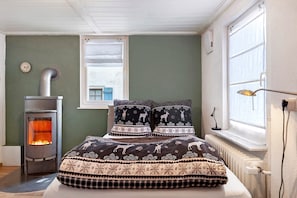 Et værelse med seng, brændeovn, et vindue og en radiator.