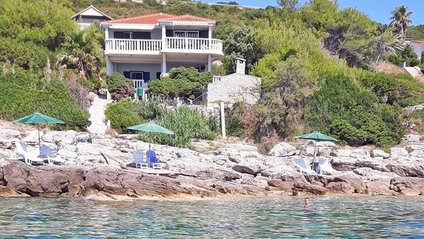 A coastal property with a two-story building, a rocky shoreline, and clear blue water. - Apartments Ruzica (Vis)