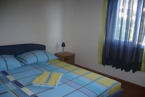 Ein Schlafzimmer mit einem Bett, einem Nachttisch, einer Lampe und einem Fenster mit Vorhängen.