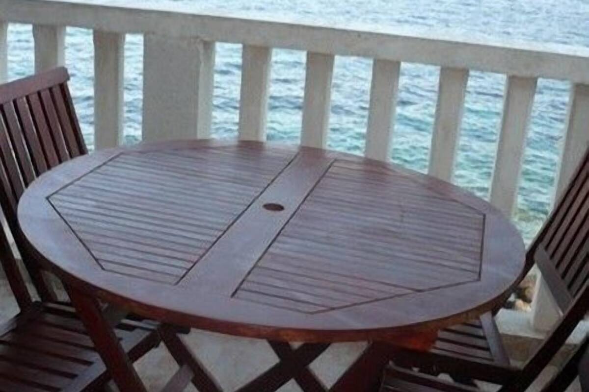 A round wooden table with four chairs on a balcony with a view of the sea.