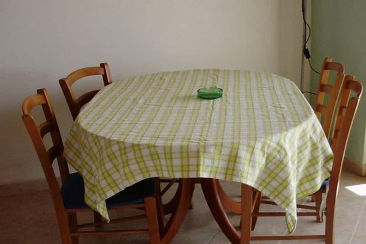 A round dining table with a checkered tablecloth, surrounded by wooden chairs.