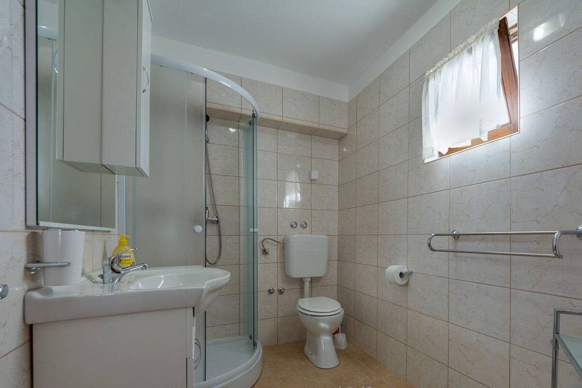 A bathroom with a glass shower enclosure, a toilet, a sink, and a mirror.