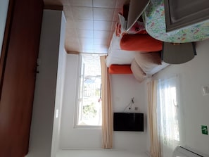Habitació amb llit, televisió penjada a la paret, finestra amb cortines i aire condicionat.