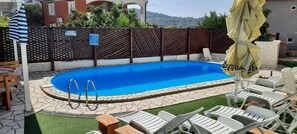 A swimming pool with a stone deck, surrounded by lounge chairs and a wooden deck. - Apartments Pemita (Rogoznica)