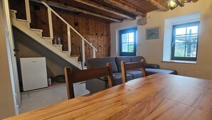 Een eethoek met een houten tafel en stoelen, een trap met een witte leuning, en een uitzicht op de omgeving door een raam.