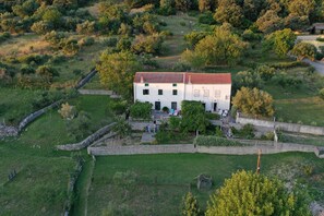 A white building with a red roof surrounded by greenery and stone walls. - House Viskic (Rab)