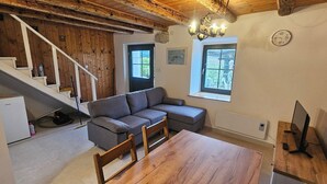 Een gezellige woonkamer met een grijze bank, een houten eettafel en een trap met houten leuningen.