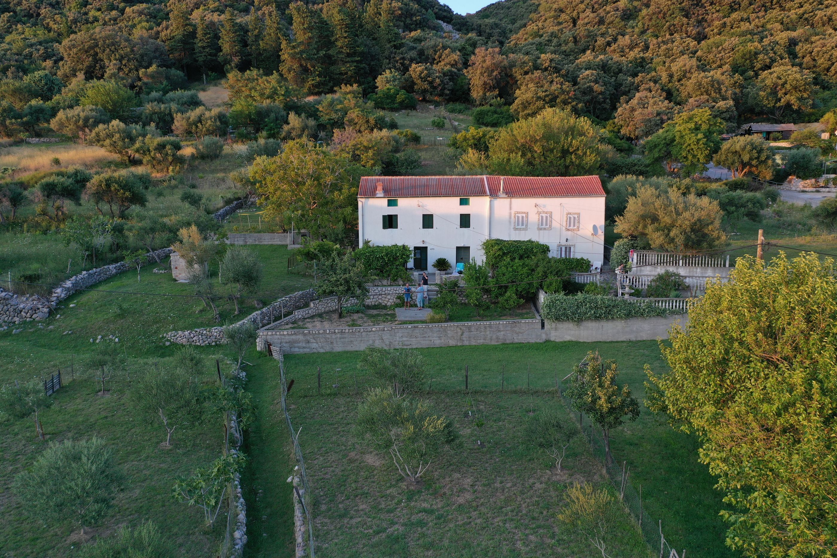 A white building with a red roof surrounded by a stone wall and greenery.