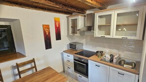 Een compacte keuken met witte kastjes, een magnetron, een spoelbak en een houten aanrecht. In de eethoek staan twee stoelen en een tafel.