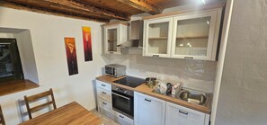 A compact kitchen with white cabinets, a microwave, a sink, and a wooden countertop. There are two chairs and a table in the dining area. - House Viskic (Rab)