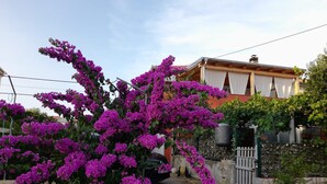 A residential area with a house featuring a stone wall, a wooden fence, and a garden with purple flowers. - Apartment Sunny Family Terrace (Povljana)