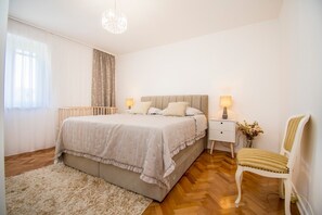 Ein Schlafzimmer mit Bett, Nachttischen, einem Sessel, einer Deckenleuchte und einem Fenster mit Vorhängen.