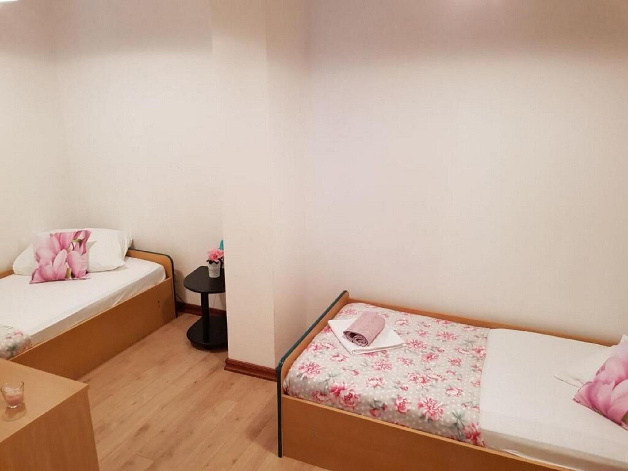 A small, clean room with two single beds, a small table, and a nightstand.