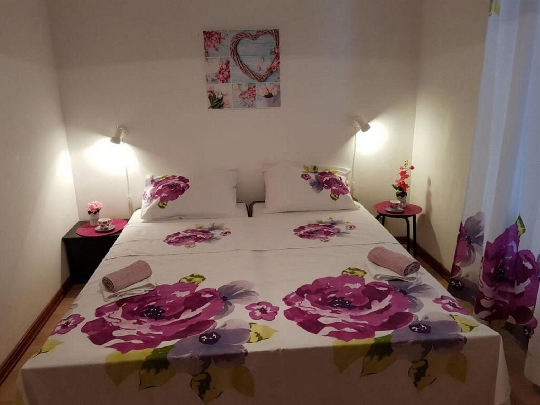 A neatly made bed with floral bedding, two bedside tables with lamps, and a wall-mounted artwork.