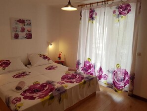 Ett sovrum med en säng, blommiga gardiner, ett sängbord och en vägglampa.