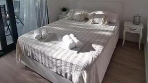 A bedroom with a large bed, a nightstand, a lamp, and a view through a glass door. - Apartments Diana Lovetovo (Vodice)