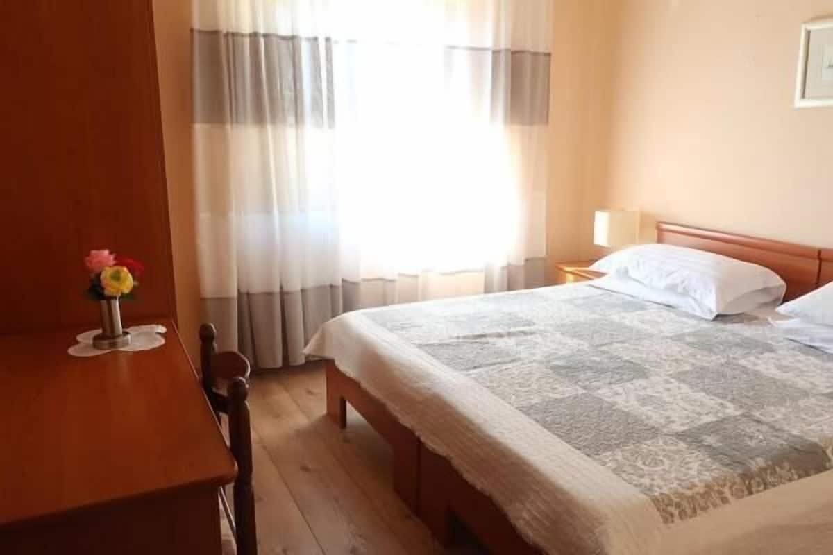 A hotel room with a bed, a wooden desk, and a vase of flowers.