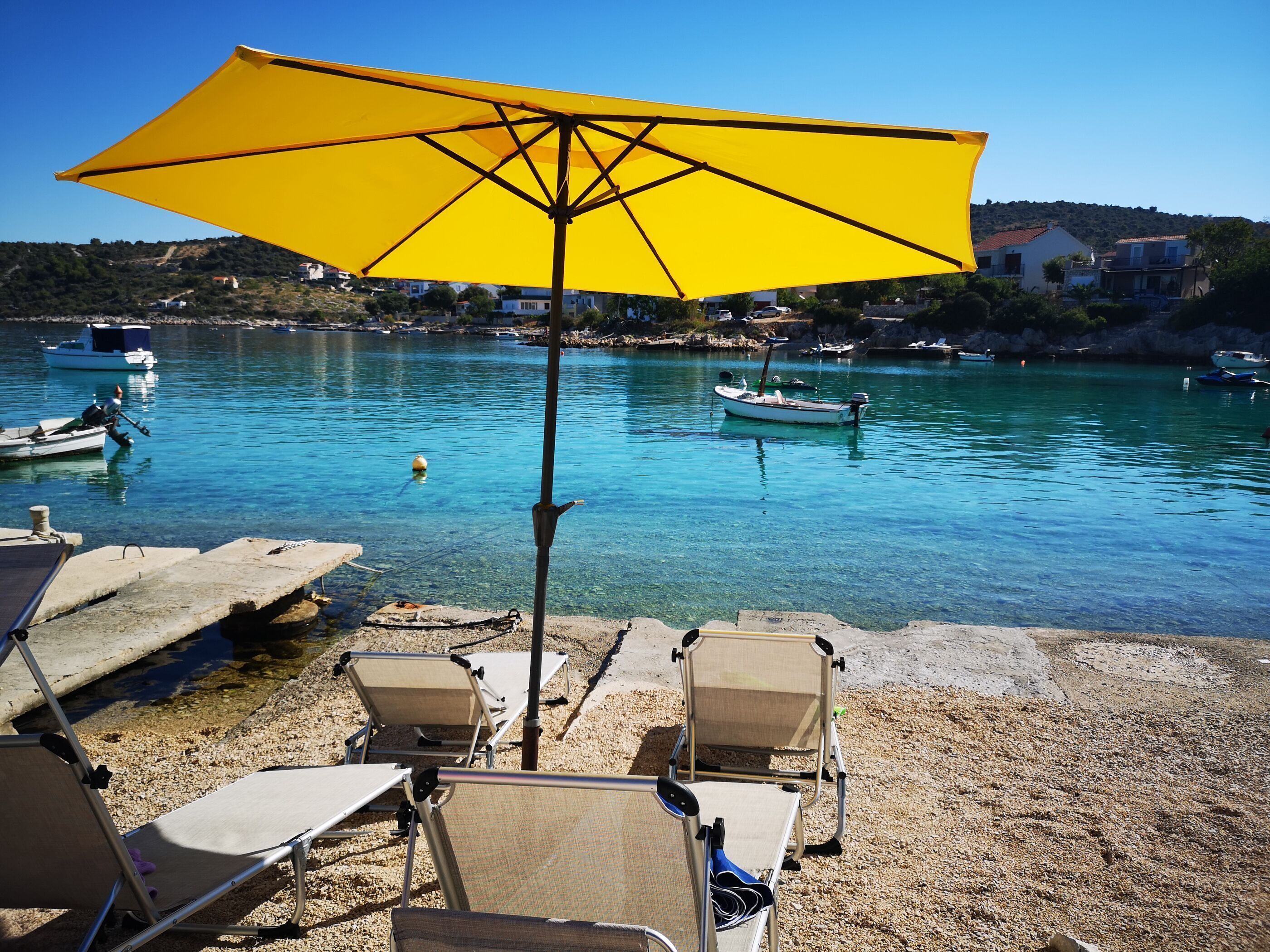 Una spiaggia con acque cristalline, un ombrellone giallo e diverse sdraio.