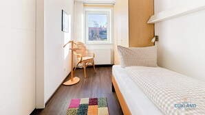Ein kleiner, heller Raum mit einem Bett, einem Sessel und einem Fenster.