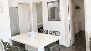 Ein Essbereich mit weißem Tisch und Stühlen, einem Spiegel und Blick in ein Schlafzimmer mit Bett und Kleiderschrank.