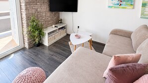 Ein modernes Wohnzimmer mit einer Couch, einem kleinen Tisch, einem an der Wand montierten Fernseher und einem Kamin aus Ziegelsteinen.