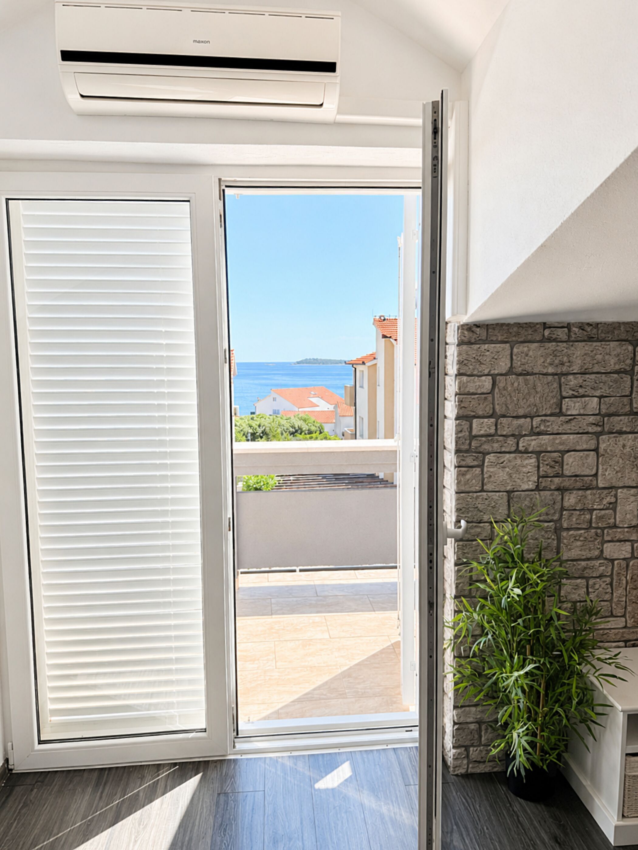 An open sliding door leading to a balcony with a view of the sea and buildings.