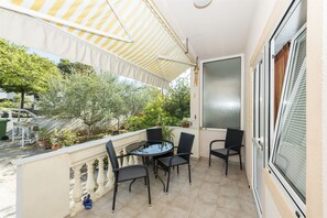A balcony with a table and chairs, a striped awning, and potted plants. - Apartment Katarina (Zadar)