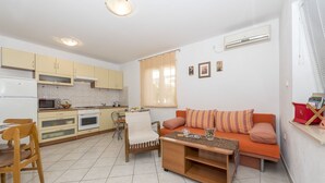 Ett kompakt bostadsutrymme med ett litet kök, en soffa med kuddar, ett soffbord och en matplats med stolar.